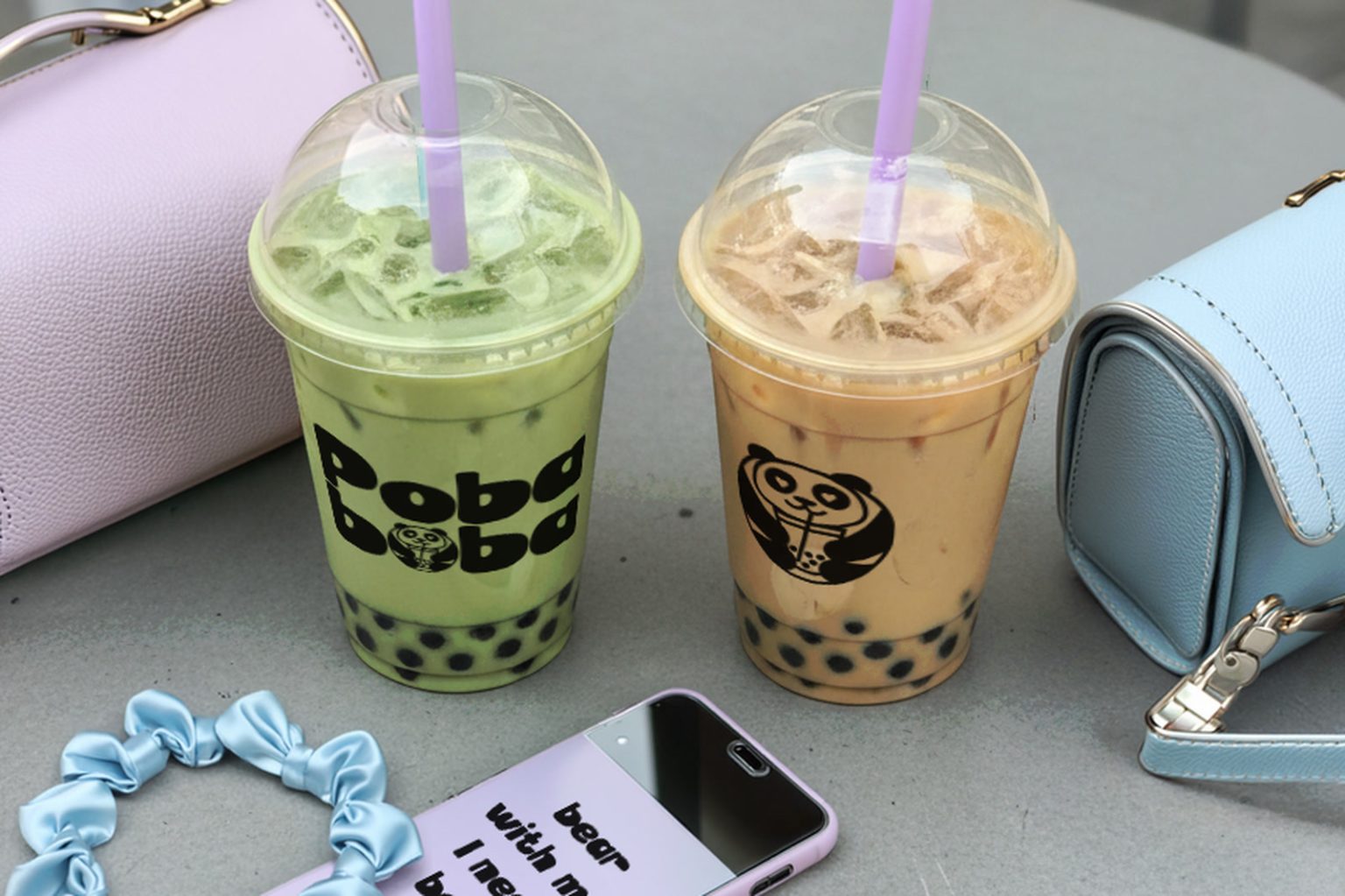 Poba Boba two bubble tea cups on a cafe table beside pastel bags and a branded phone case